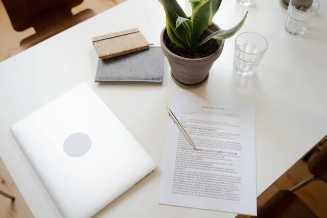 Top view of a clean workspace with laptop, contract, and plant for productivity and focus. Untermiete von Geschäftsräumen: Zustimmung und Grenzen